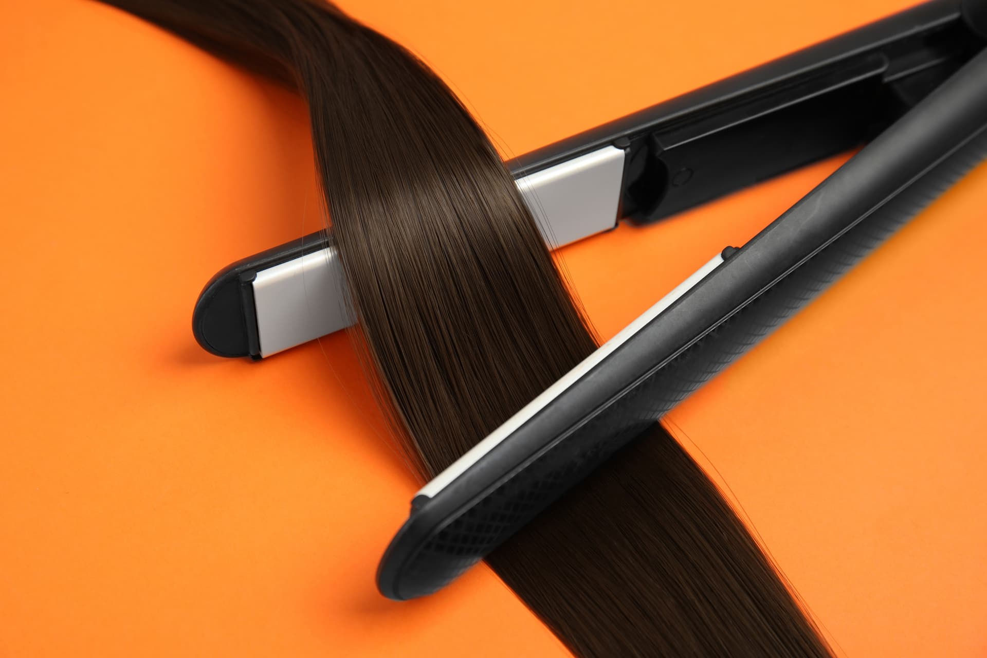 straightener-with-brown-hair-lock-on-orange-backgr-2026-01-16-21-34-56-utc.jpg